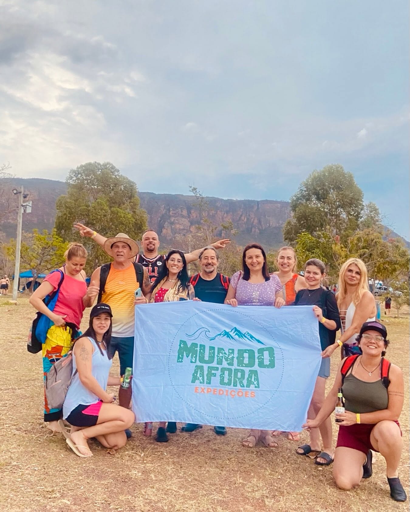 Grupo da Mundo Afora Expedições com a bandeira da equipe em frente à serra